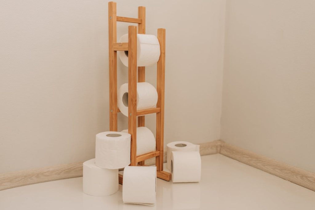 Neatly stacked toilet paper rolls on a bamboo rack in a minimalist bathroom corner.